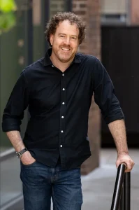 Steve Sheinkin white man standing in black button up shirt with short brown curly hair